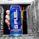 A hand grabs a blue G Fuel energy drink can out of a fridge filled with black and white gans.